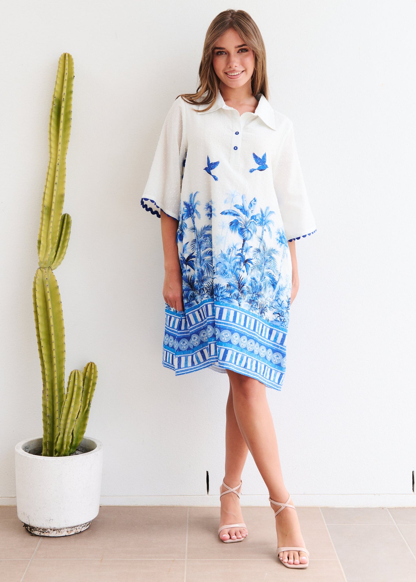 Woman wearing a floral dress standing next to a cactus plant indoors.