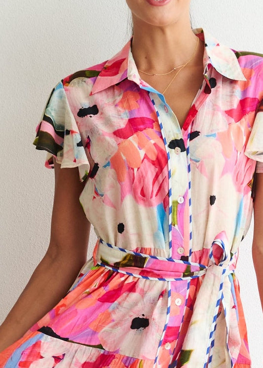 Woman wearing a colorful floral dress standing in a room with a chair and white wall.
