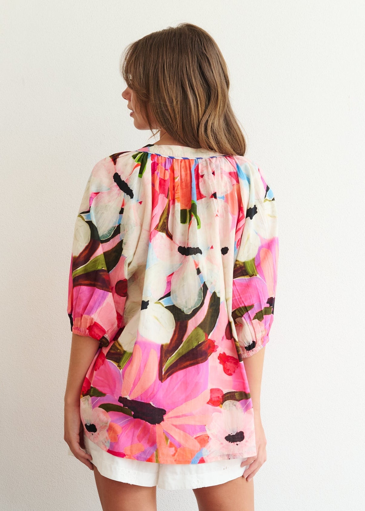 Woman wearing a colorful floral blouse standing in a minimal room.