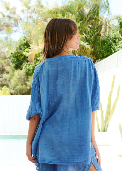 Woman wearing a blue cover-up standing in a bright room with large windows.