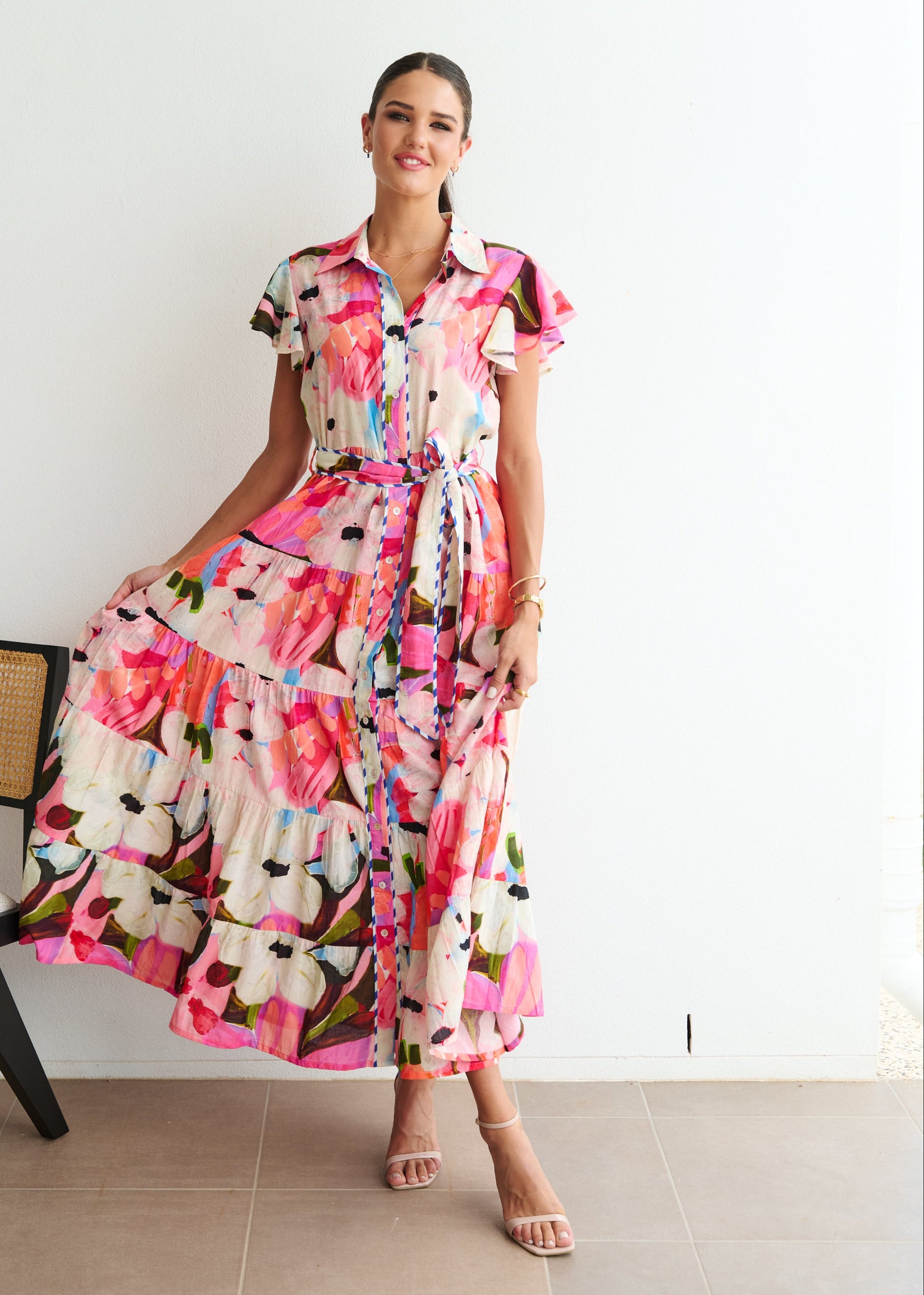 Woman wearing a colorful floral dress standing against a white wall.