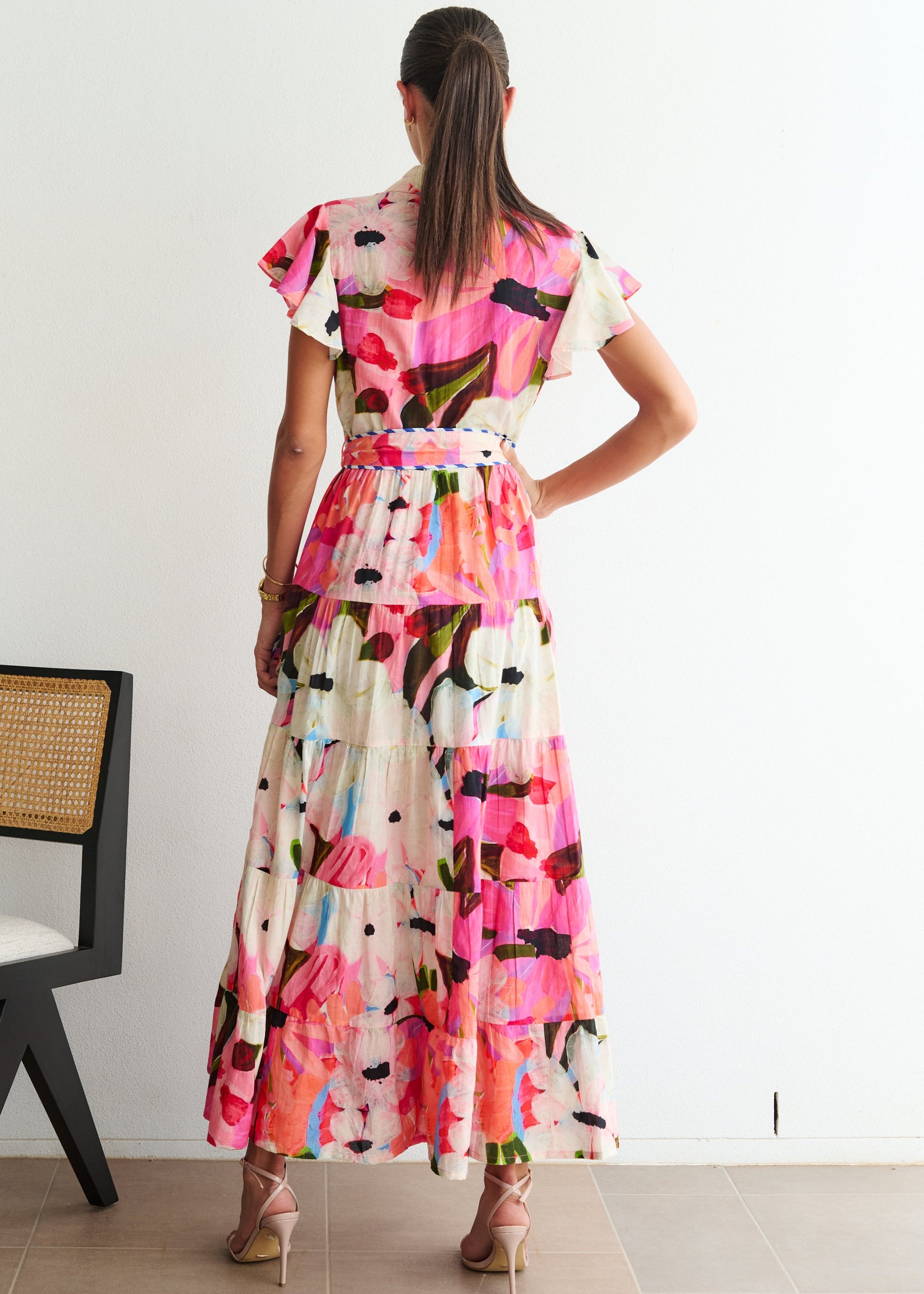 Woman wearing a colorful dress standing in a room with a chair and white wall.