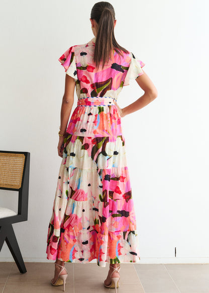 Woman wearing a colorful dress standing in a room with a chair and white wall.