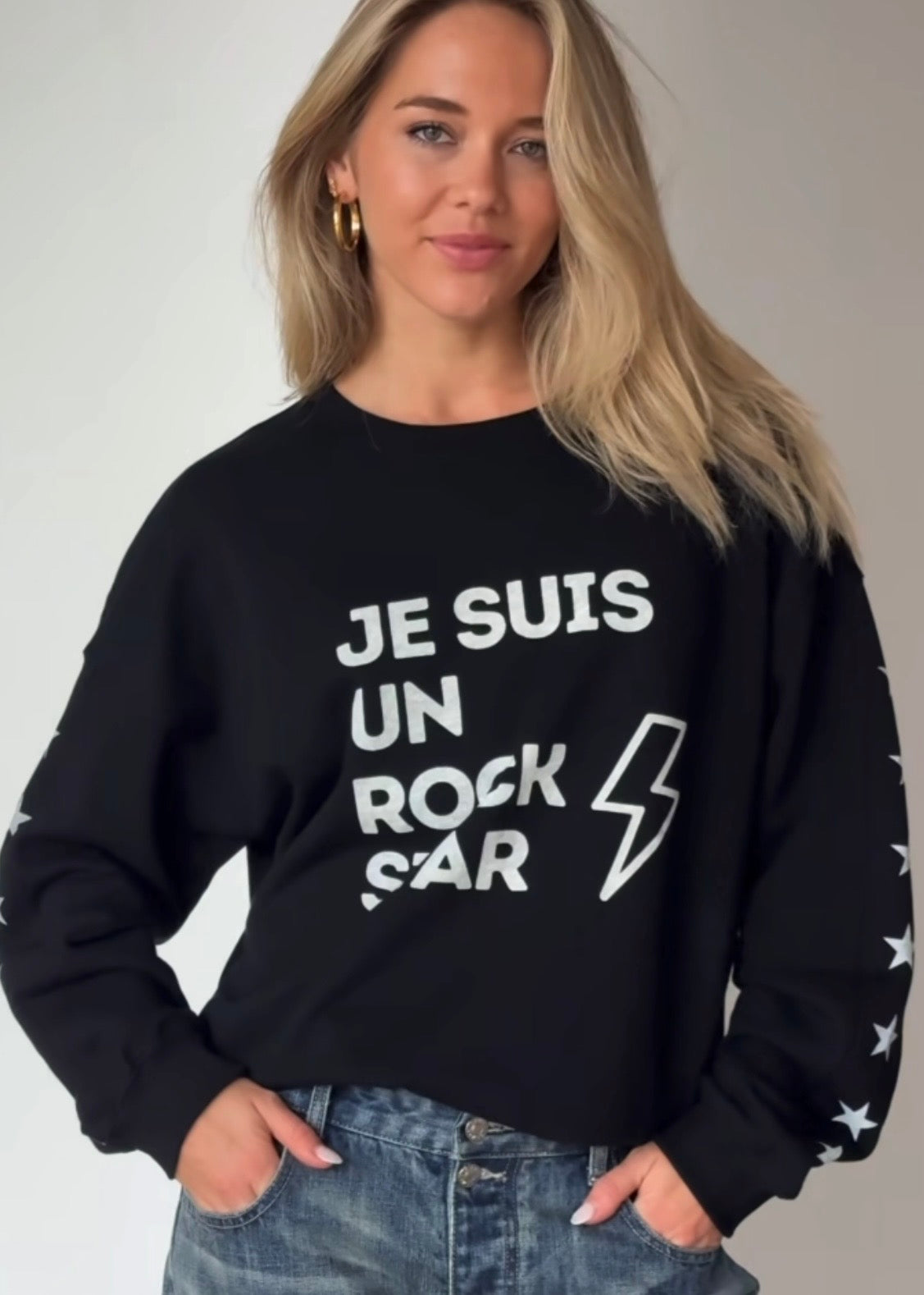 Woman wearing a black sweatshirt with text Je suis un rockstar graphic