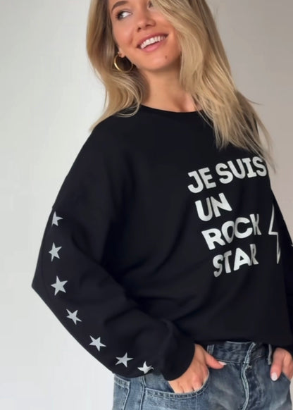 Woman wearing a black sweatshirt with text Je suis un rockstar graphic