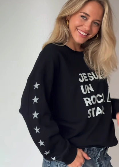 Woman wearing a black sweatshirt with text Je suis un rockstar graphic
