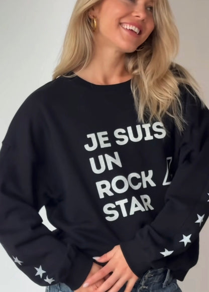 Woman wearing a black sweatshirt with text Je suis un rockstar graphic