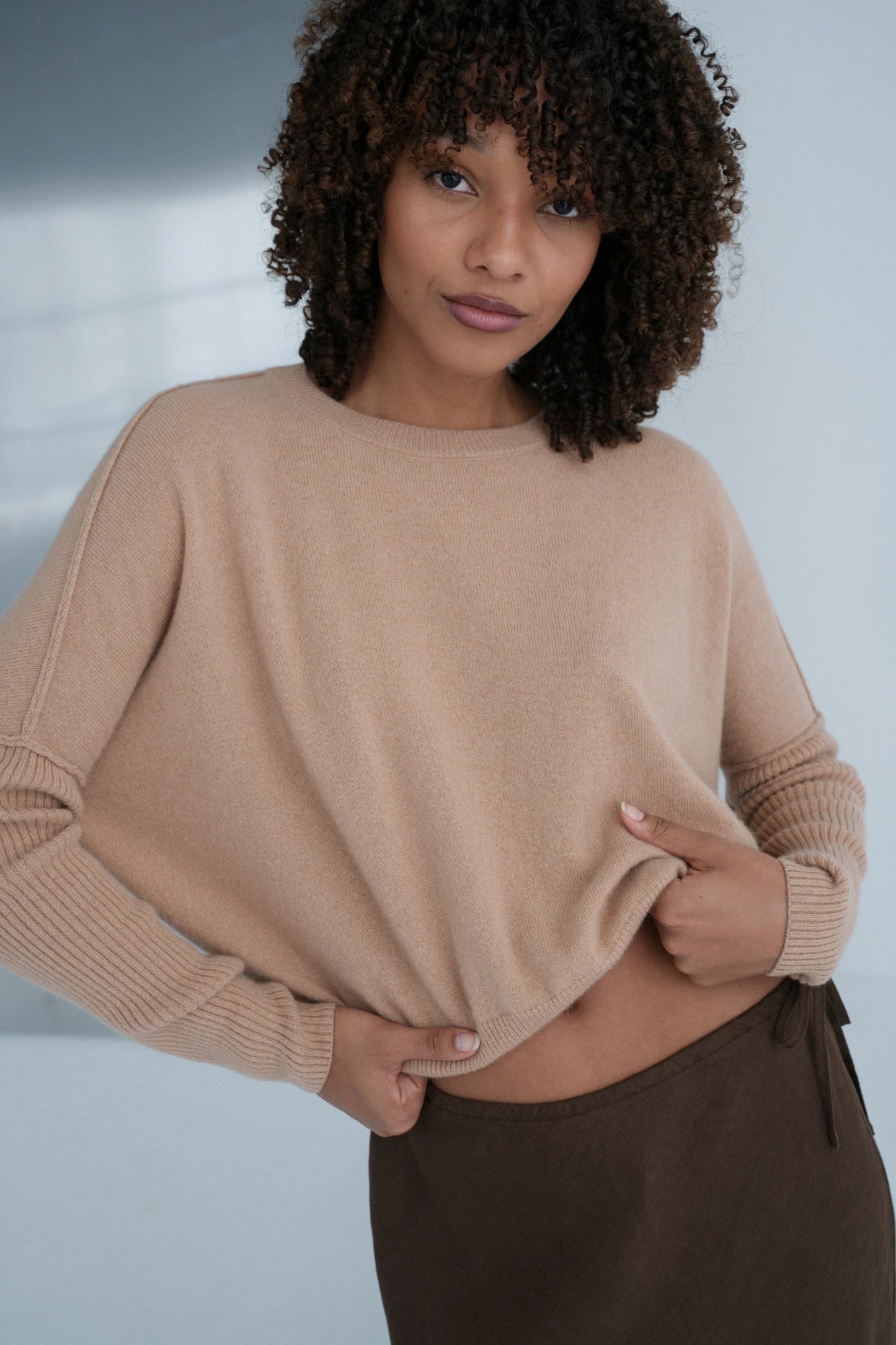 Woman wearing a beige cashmere sweater and brown pants against a neutral background