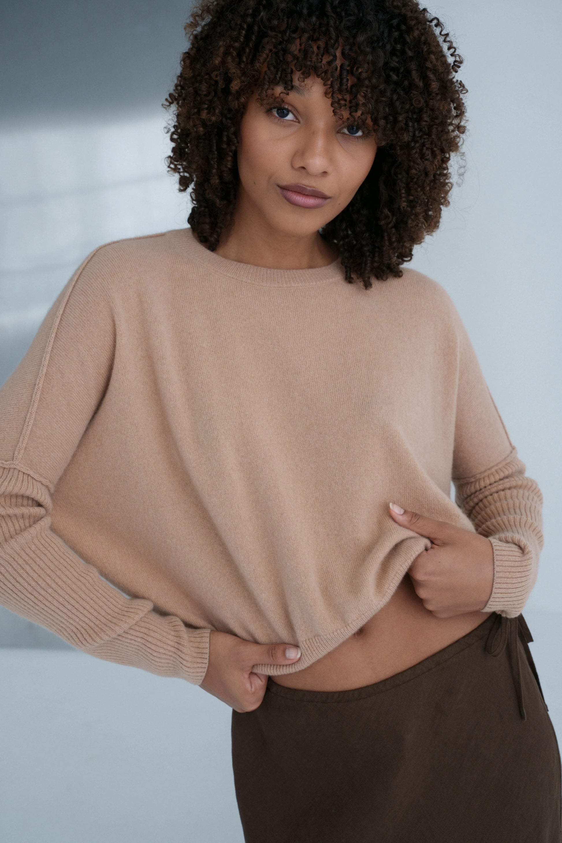 Woman wearing a beige cashmere sweater and brown pants against a neutral background