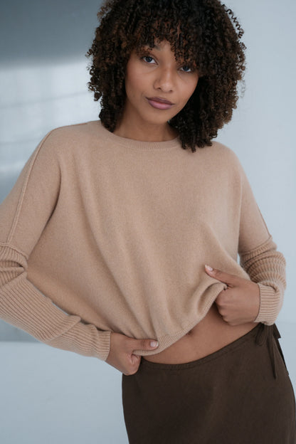 Woman wearing a beige cashmere sweater and brown pants against a neutral background