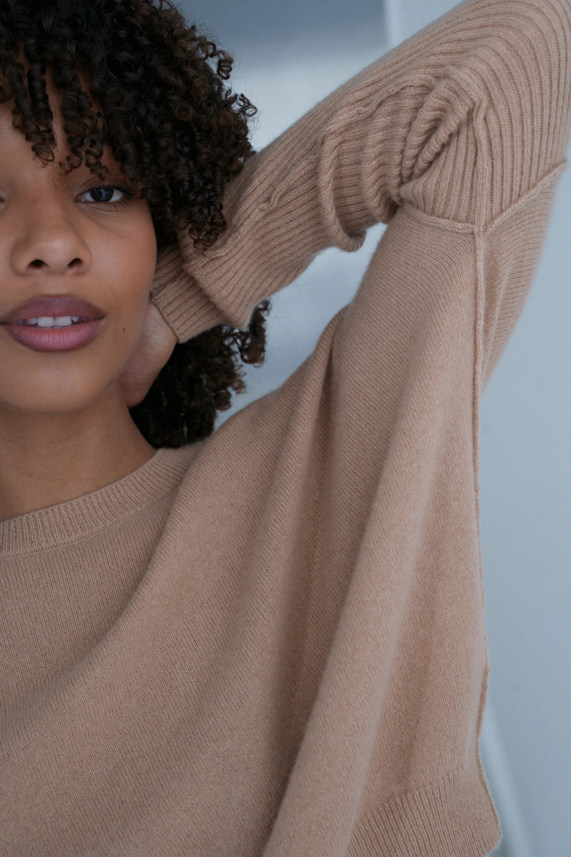 Woman wearing a beige cashmere sweater and brown pants against a neutral background close up detail