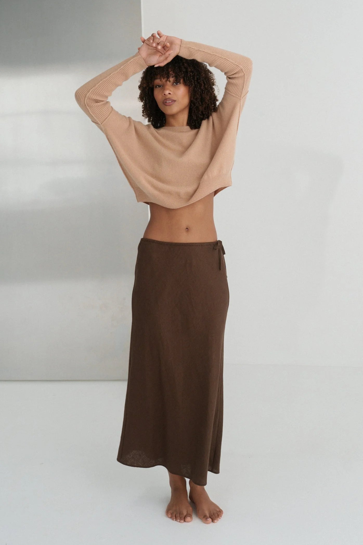 Woman wearing a beige cashmere top and brown skirt against a white background