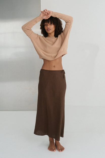 Woman wearing a beige cashmere top and brown skirt against a white background