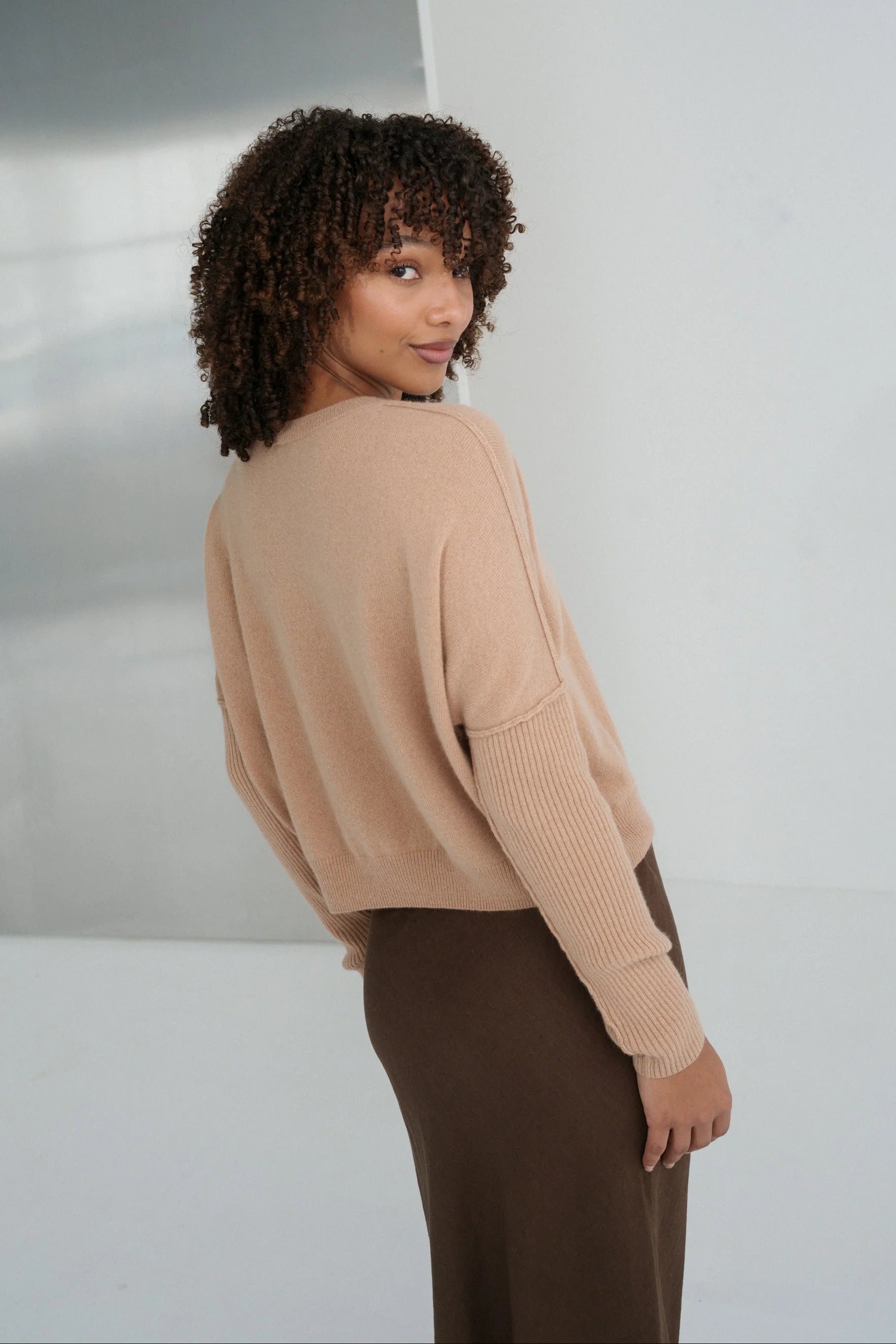 Woman wearing a beige cashmere sweater and brown pants against a neutral background