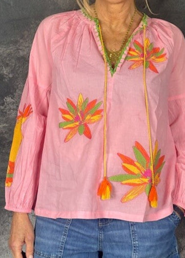 Woman wearing a pink blouse with floral embroidery against a dark background